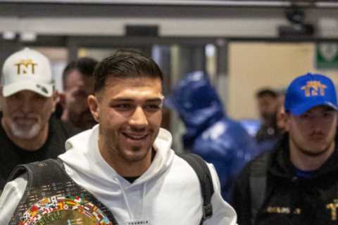 Bruised Tommy Fury beams as he touches down at Heathrow with brother Tyson and dad John after huge win over Jake Paul